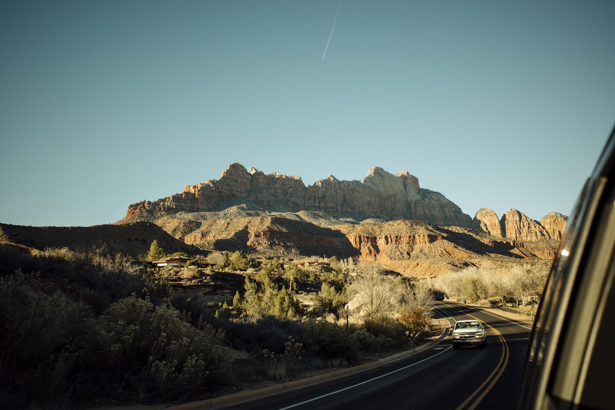 An open road running toward rocky mountains under a clear blue sky, a road-trip view with no identifiable people and no readable brands or plates, for the piece on where a family trip's savings are real