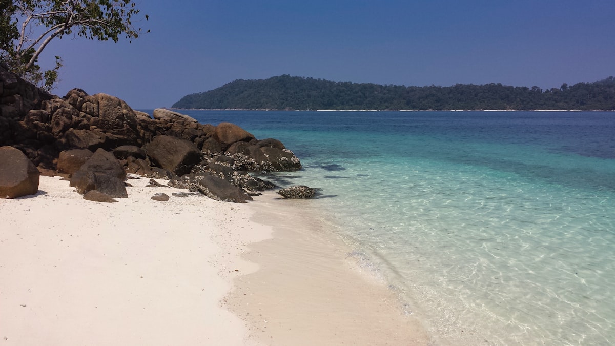 An empty white-sand beach with clear turquoise water and rocks on Ko Rawi, an uninhabited island in Mu Ko Tarutao national park beside Ko Lipe, no people and no branding, for the piece on Ko Lipe's overdevelopment and Urak Lawoi displacement