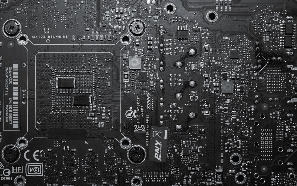 A close-up of a graphics card's circuit board in black and white, foregrounding the chips and memory rather than any branded shroud, no prominent logo, for the piece on GPU prices driven by the AI memory boom
