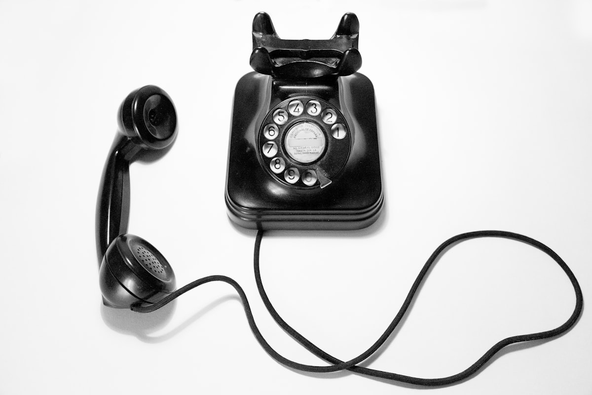 A black rotary dial telephone on a white surface, no identifiable people, standing in for the impersonation phone call at the center of the voice-clone scam piece