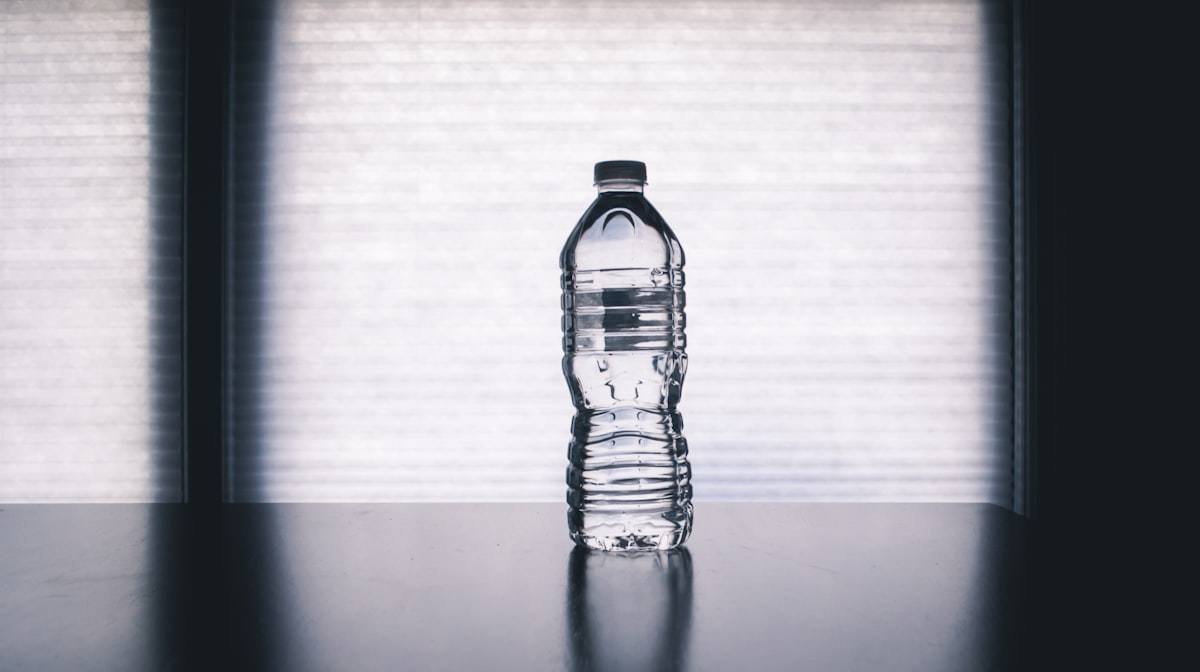A single clear plastic bottle filled with water on a plain background, no people and no readable brand or logo, a calm everyday-exposure image for the sober piece on microplastics found in human brains and artery plaque