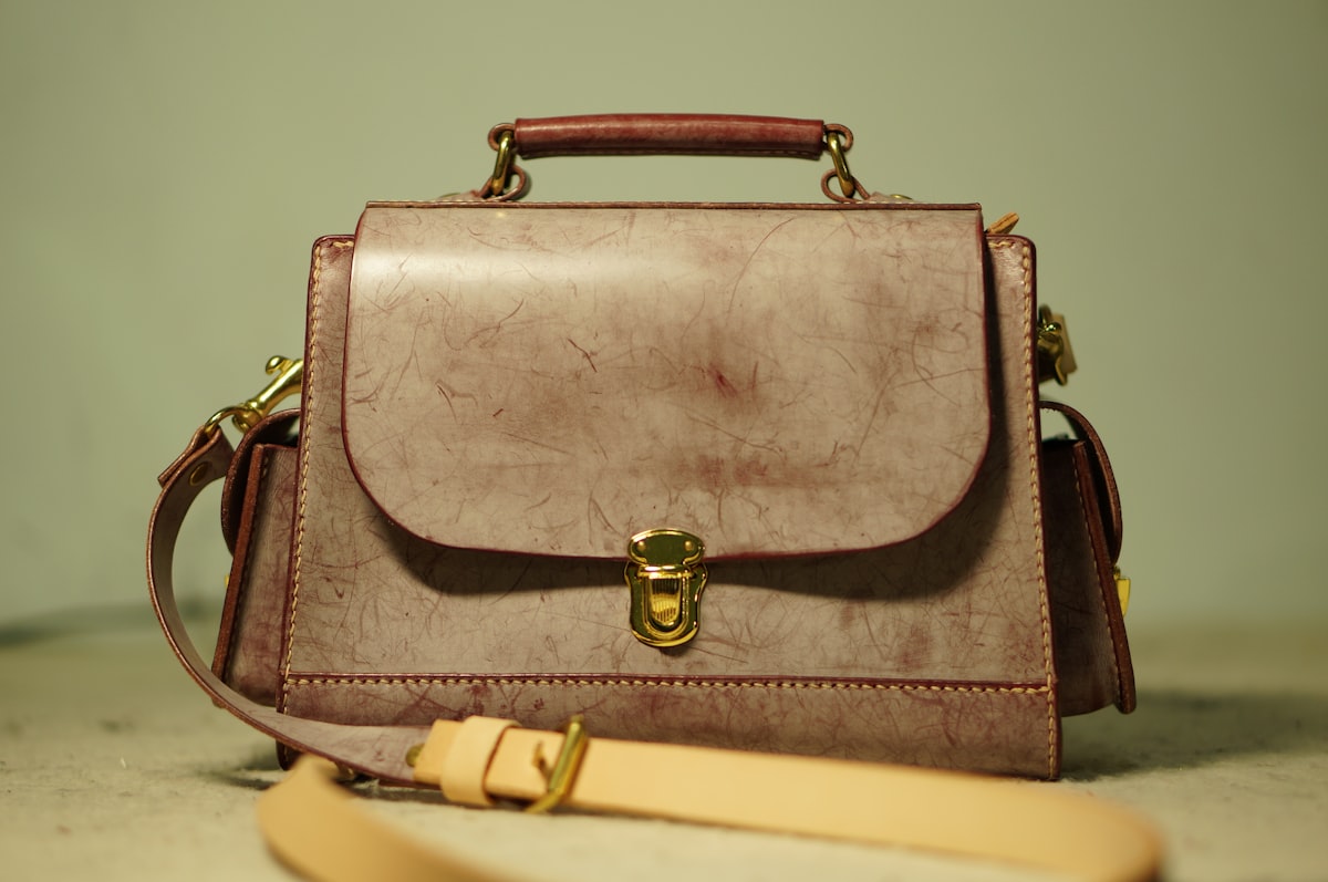 A generic unbranded taupe structured leather satchel with a gold push-lock clasp as a still life on a plain surface, explicitly not a Hermes or Birkin, no readable brand or logo and no identifiable people, for the piece on a record Birkin auction sale against handbags falling as an asset class