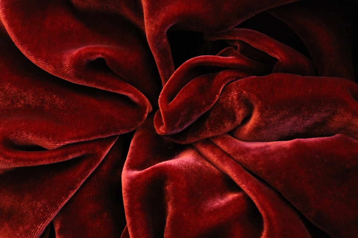 A close still life of deep crimson velvet folded and swirled into soft ridges, catching low light, no identifiable people and no readable brand or logo, for the piece on romantic maximalism bringing velvet and jewel tones back for fall