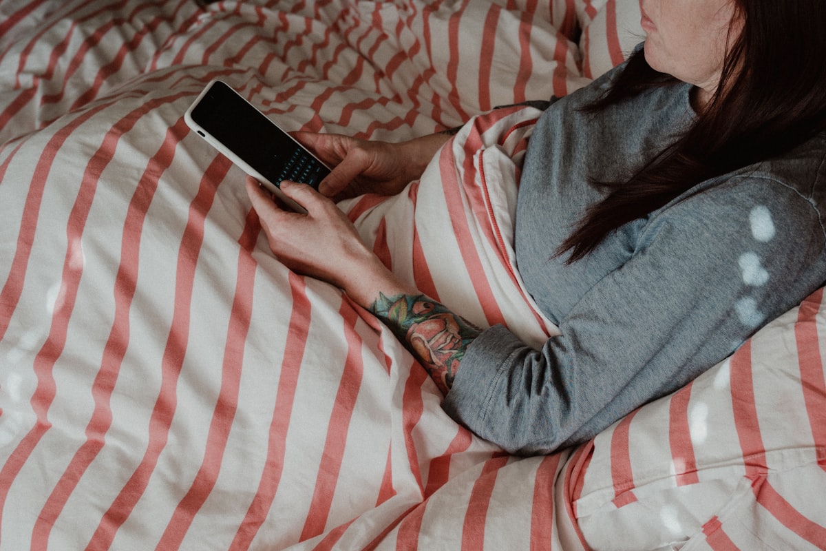 A person lying on a bed doing the morning phone scroll, no face shown, for the piece on over-reading nightly sleep-tracker data and the anxiety it breeds