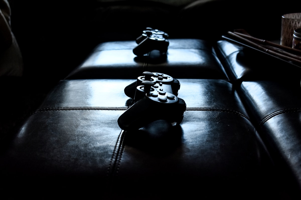 Two dark game controllers resting on a leather ottoman in low light, no identifiable person and no readable brand or logo, for the piece on Halo going multiplatform and the end of console exclusivity