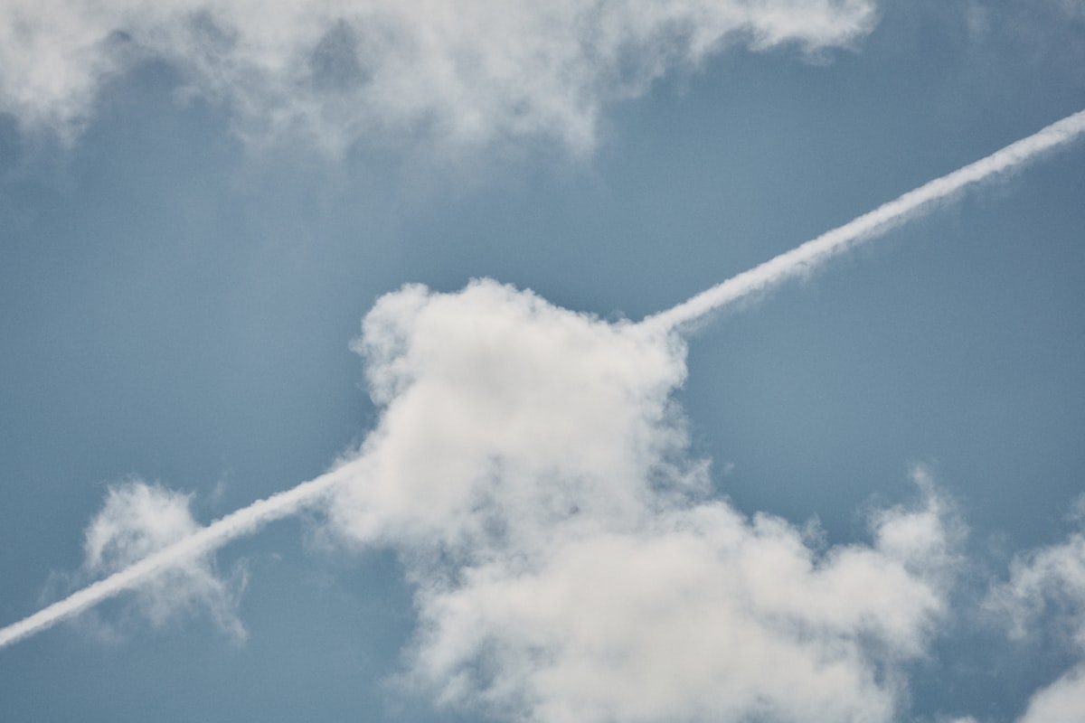 A single airplane contrail drawn across a cloudy blue sky, no aircraft livery, brand, logo, or identifiable people, carrying the carbon-in-the-air motif for the piece on Qantas's 22-hour nonstop