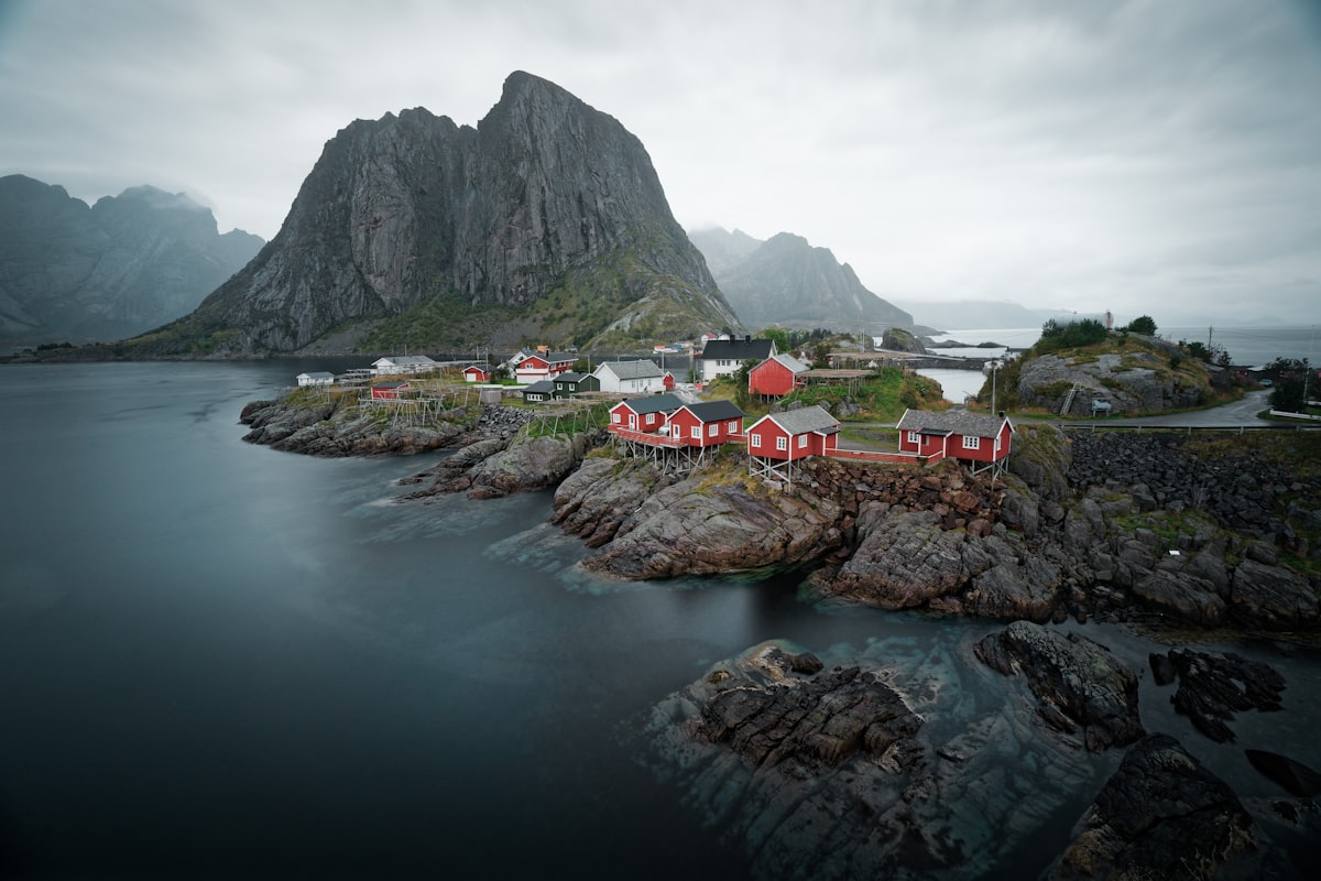 Red fishing cabins on rocky islets below a steep peak in the Lofoten islands of Norway, calm water in the foreground, no identifiable people and no readable brands or logos, for the piece on the coolcation trend