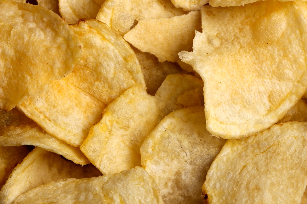 An overhead close-up of a pile of plain potato crisps with no packaging, no identifiable people and no readable brands or logos, for the piece on ultra-processed food and disease
