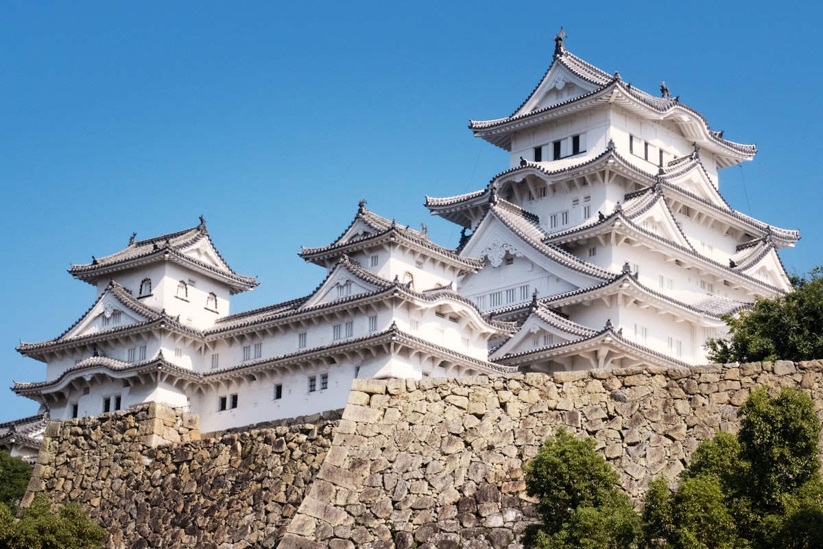 The white keep of Himeji Castle in Japan rising above its stone walls against a blue sky, no identifiable people and no readable commercial brands or logos, for the piece on Japan's resident-and-tourist two-tier pricing